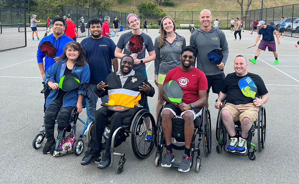 Group of individuals standing and in wheelchairs on a pickleball court
