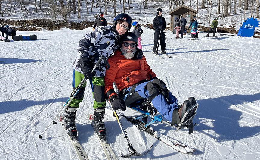 Man snow skiing with assistance and adaptive equipment