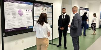 Medical student presenting and speaking about his research poster to two people