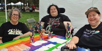three women sitting at a booth for pittsburgh disability pride